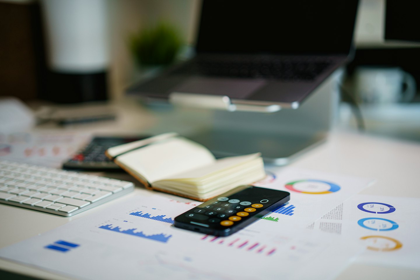Laptop, keyboard, notebook, and smartphone on a desk with financial charts.